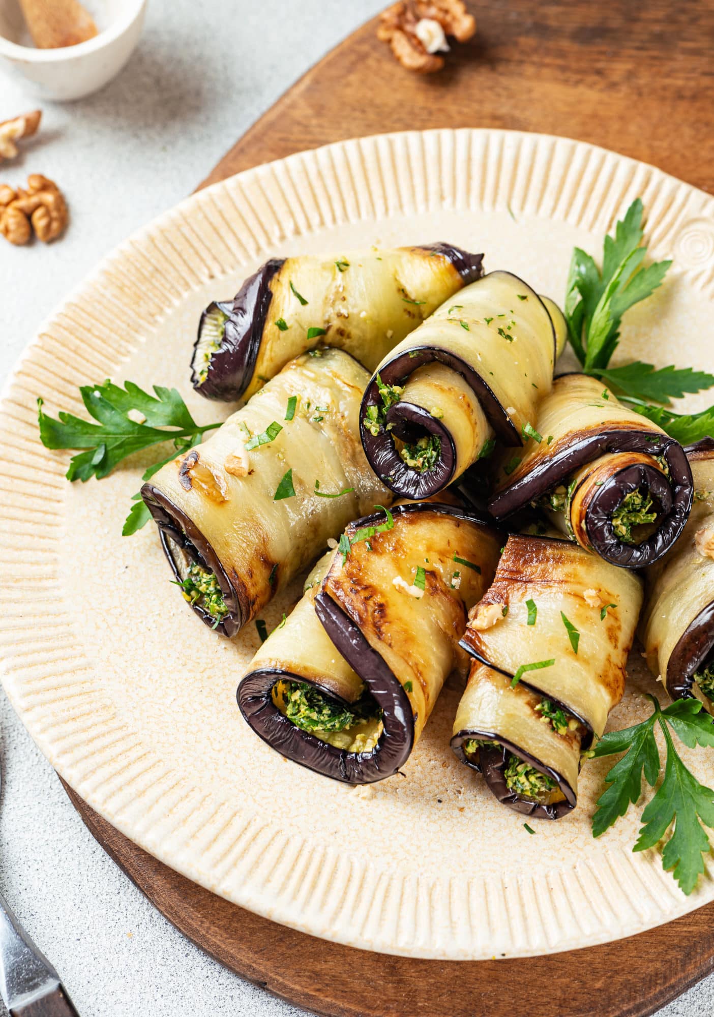 eggplant rolls filled with herbs with parsley leaves on the sides on a beige plate.