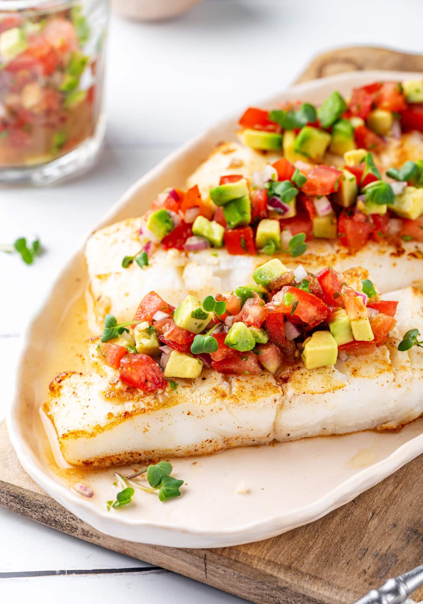 A seared piece of halibut on a white plate with salsa on top.