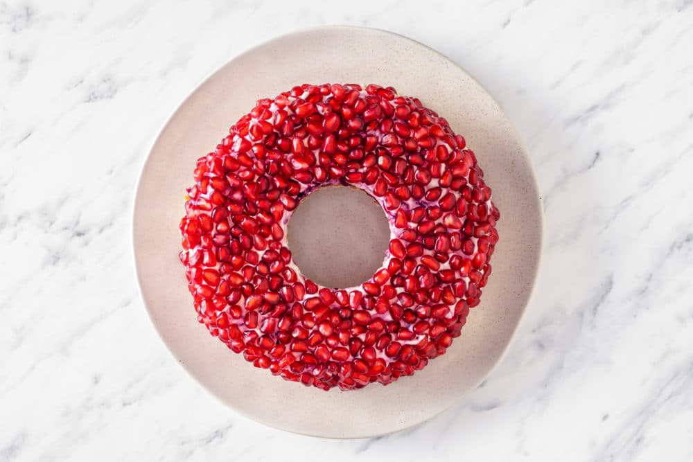 final pomegranate layer on a round wreath salad on a white plate.