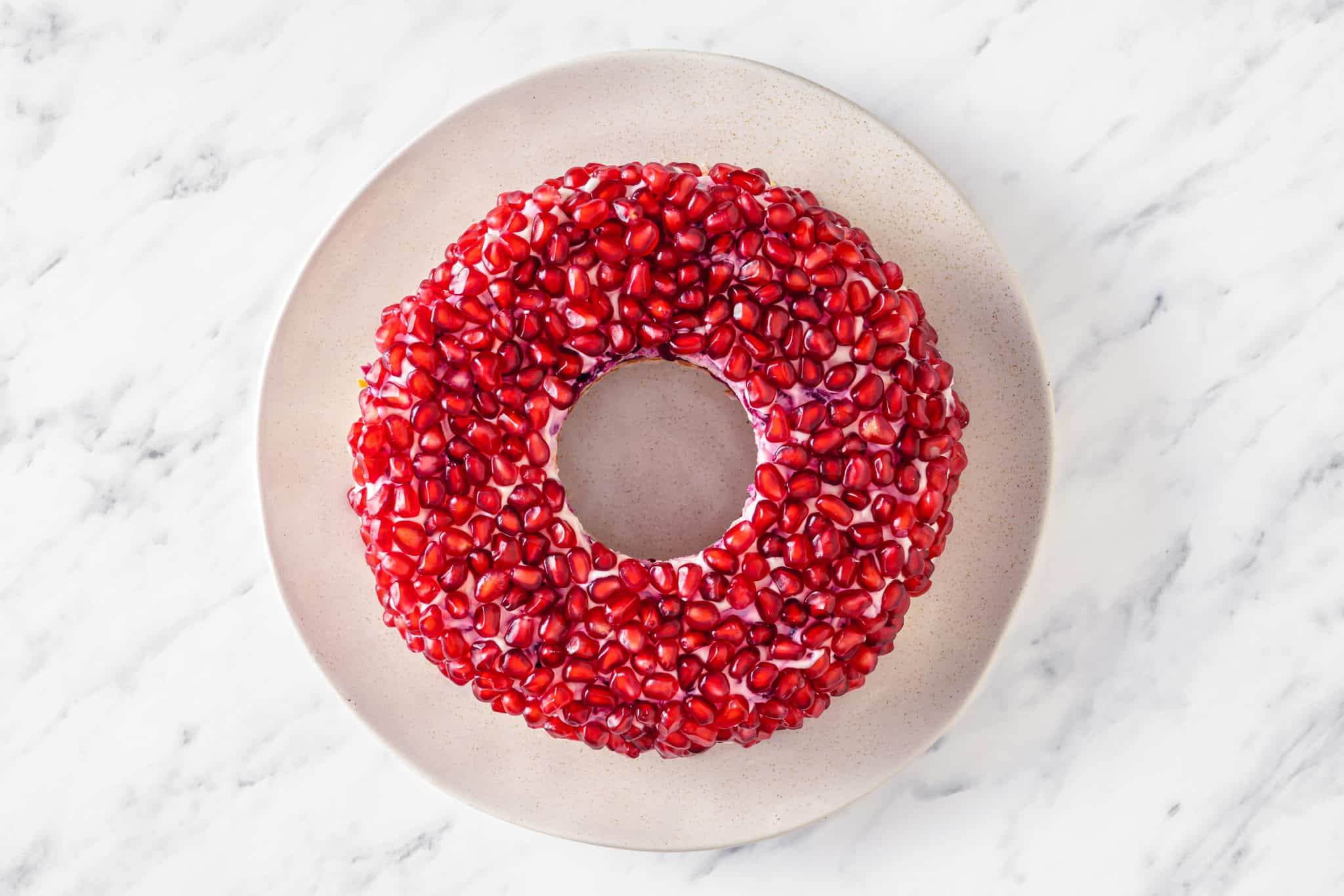 final pomegranate layer on a round wreath salad on a white plate.