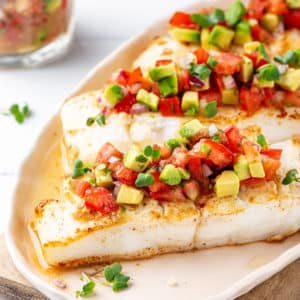 A seared piece of halibut on a white plate with salsa on top.