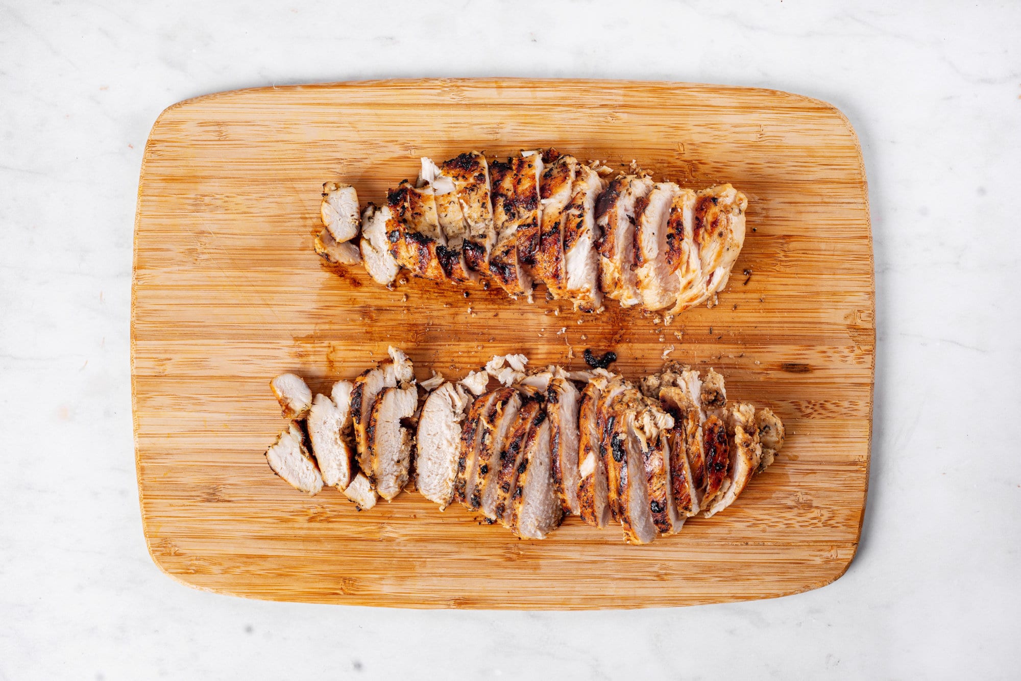 Sliced grilled chicken on a wooden board.