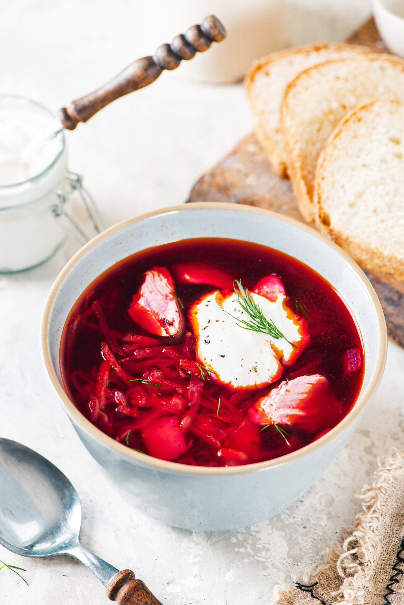 A bowl of borscht with a dollop of sour cream on top with a spoon on the side.