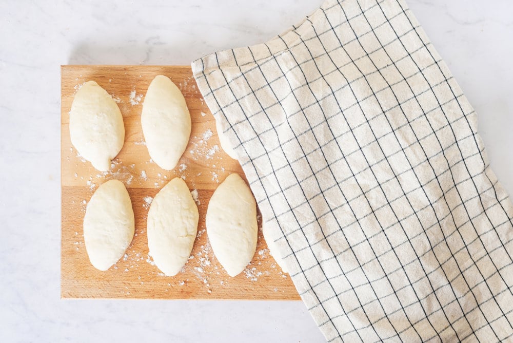 raw-piroshki-on-a-wooden-board-half-covered-by-a-white-towel