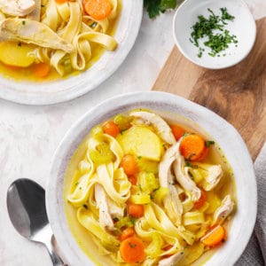 chicken-soup-in-a-white-bowl-on-a-wooden-board-with-a-spoon