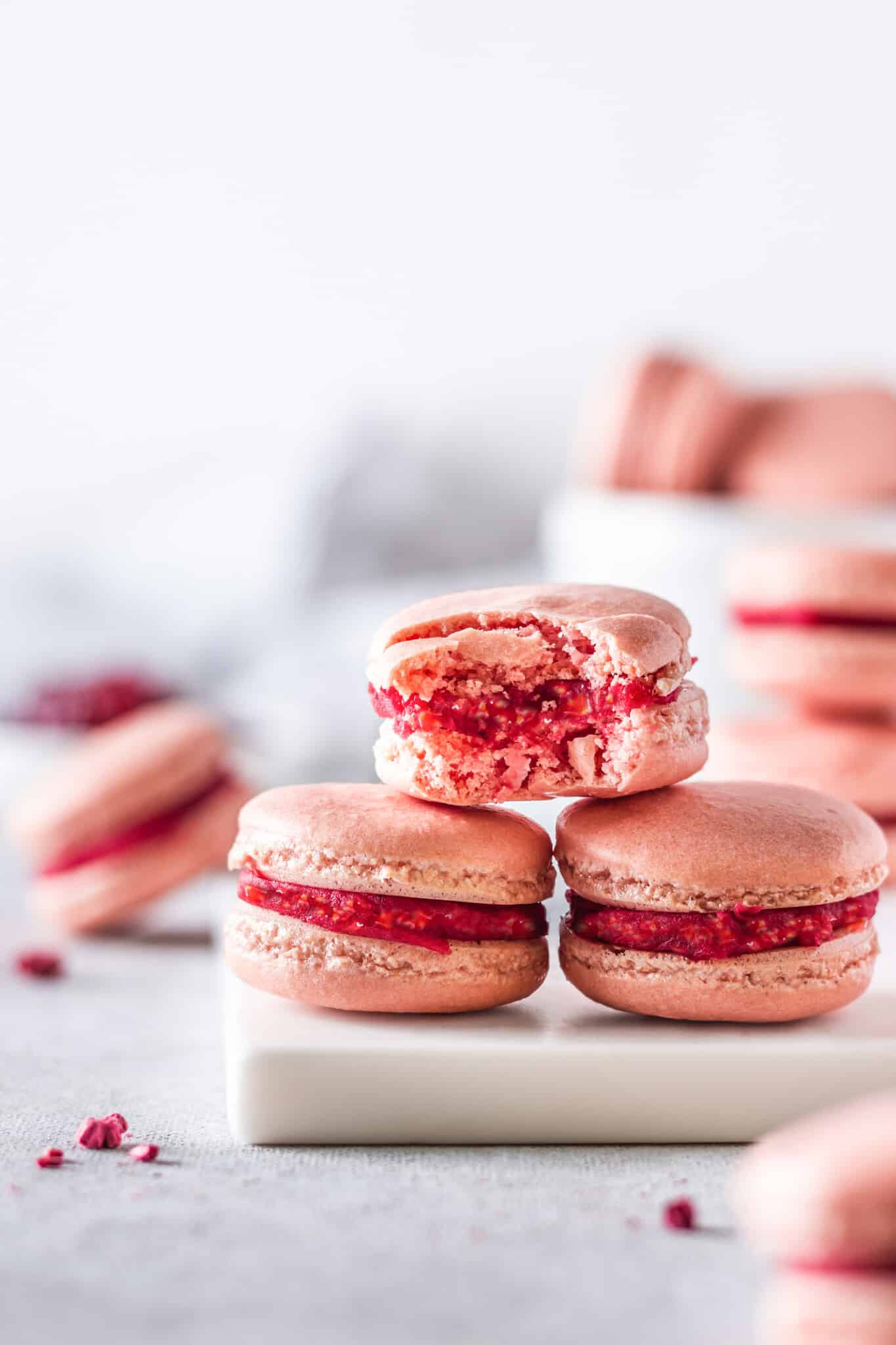 Stacked raspberry macarons on a white board with a bite taken out.