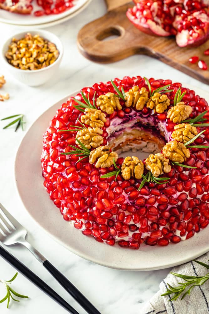 a white plate with layered wreath shaped salad on it with pomegranate as the outside layer.