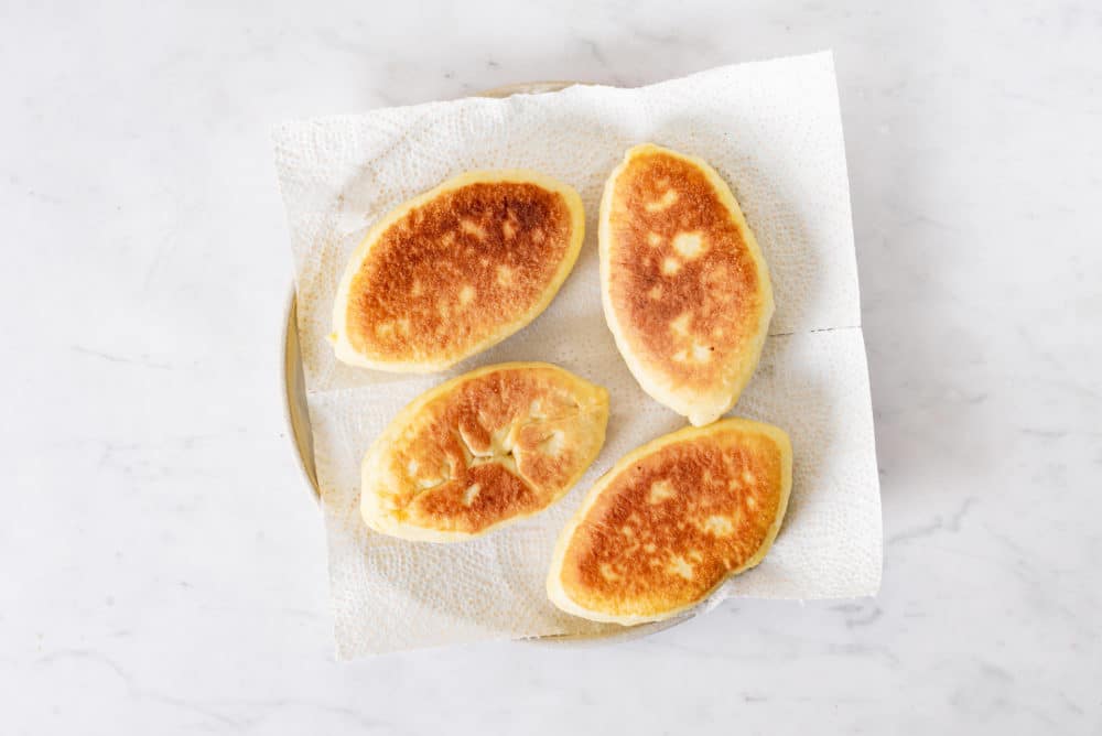 Piroshki with mashed potato filling on a plate lined with a sheet of paper towel.