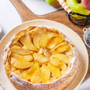 Apple cake on a white plate, on a wooden cutting board.