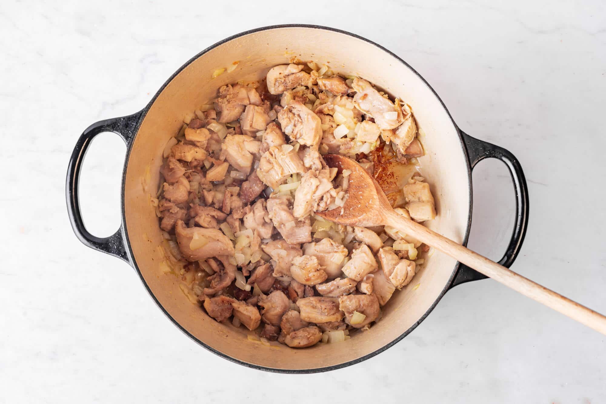 Chicken and onion sauteing in a pot with a wooden spoon.