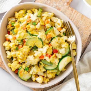 Cauliflower rice in a bowl with a fork on the side on a wooden board.