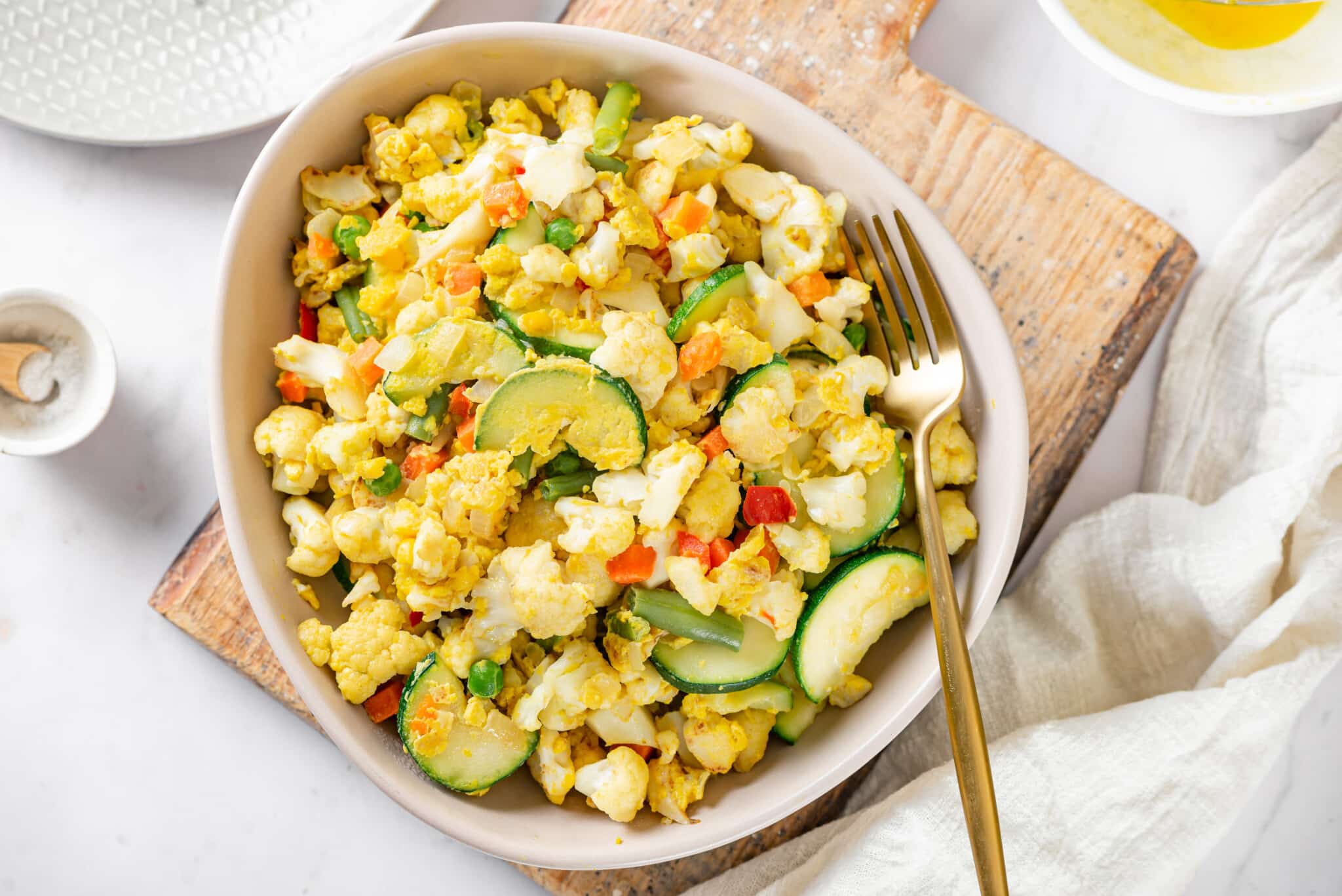 Cauliflower rice in a bowl with a fork on the side on a wooden board.