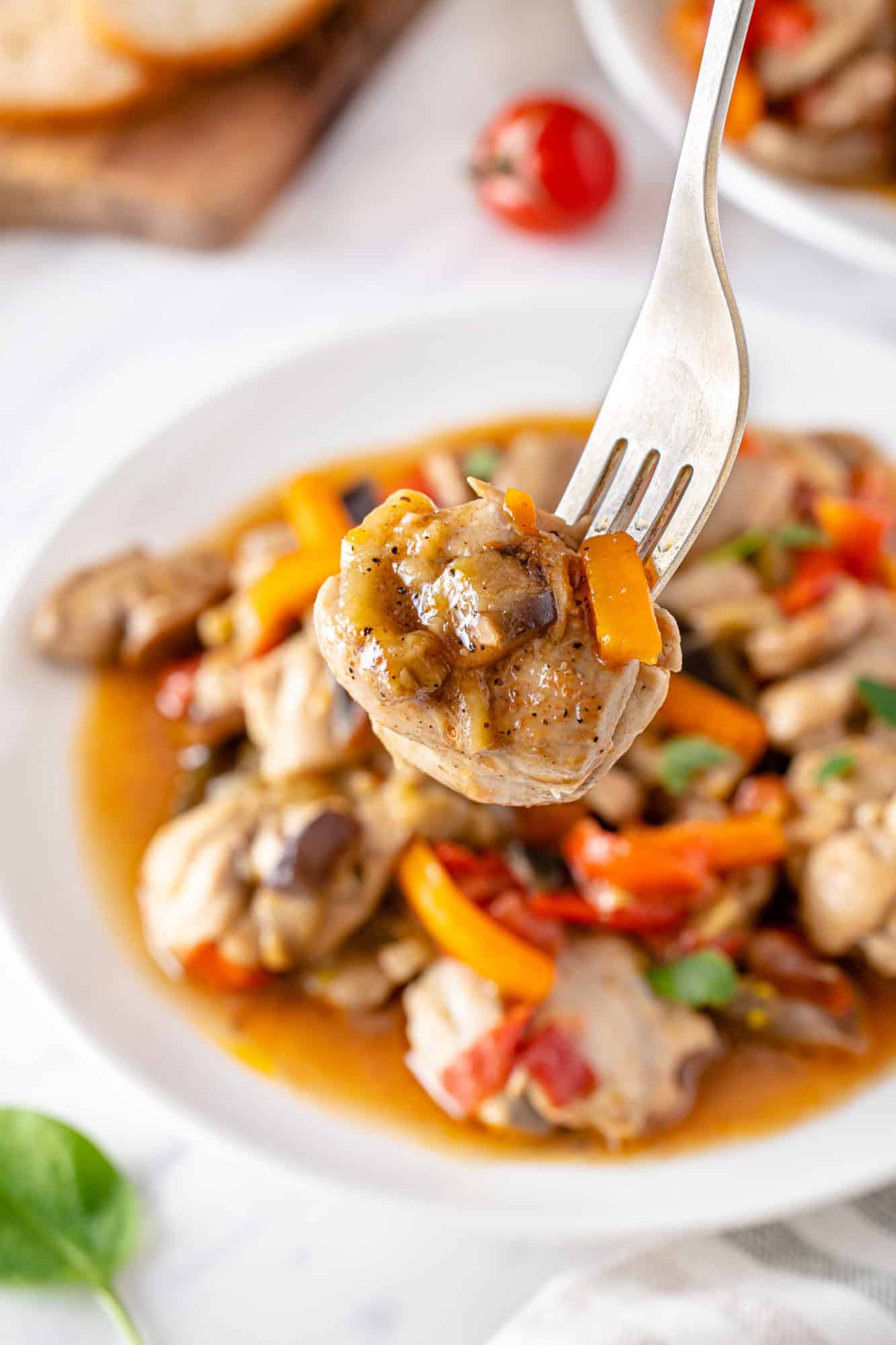 a fork with some sauteed chicken and veggies on it with more on a white plate.