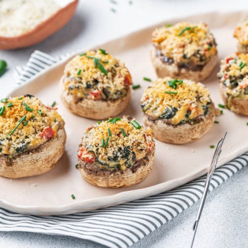 a striped towel with a beige plate on it and stuffed mushrooms prepared.