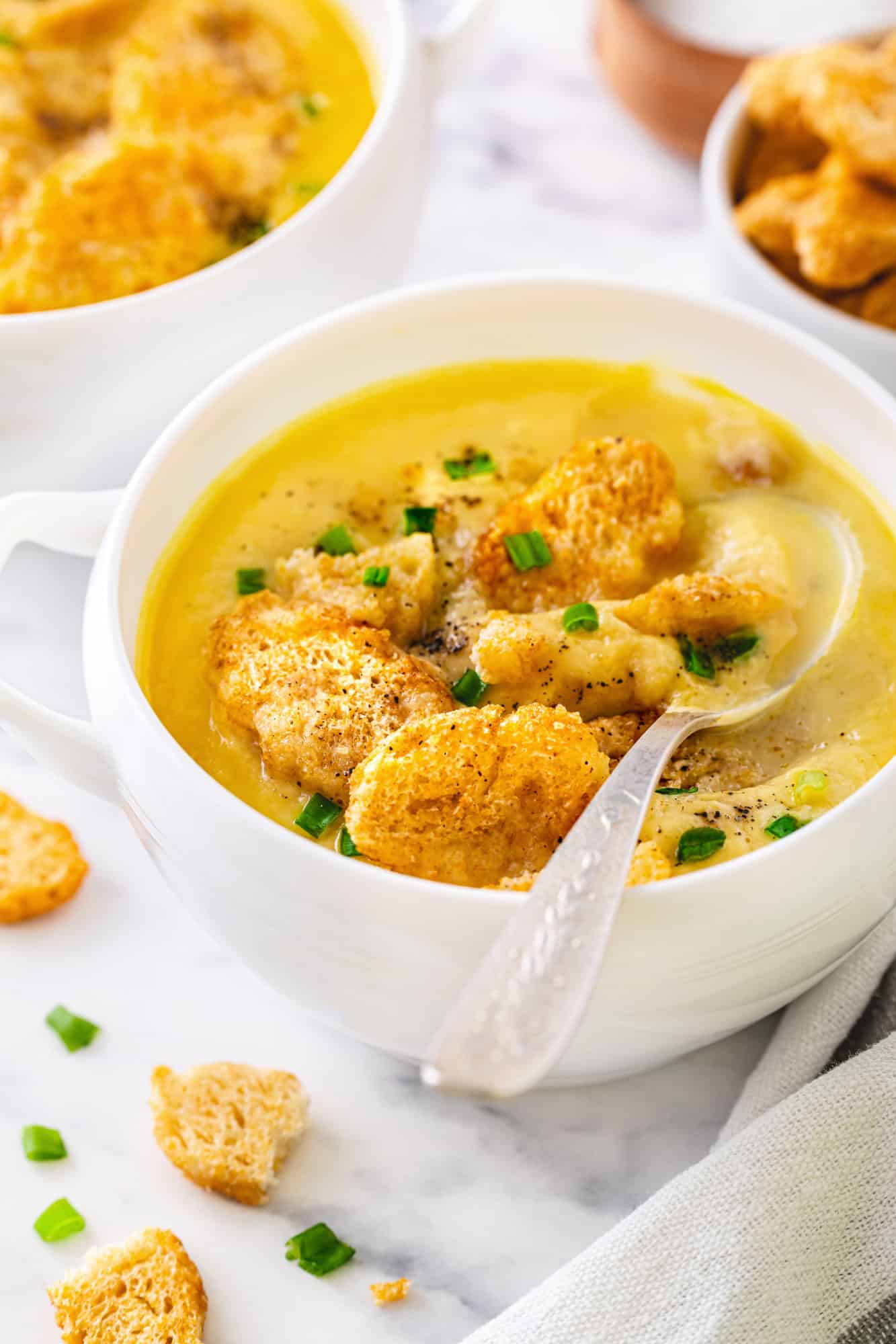 a white bowl of creamy cauliflower soup with croutons and a spoon.