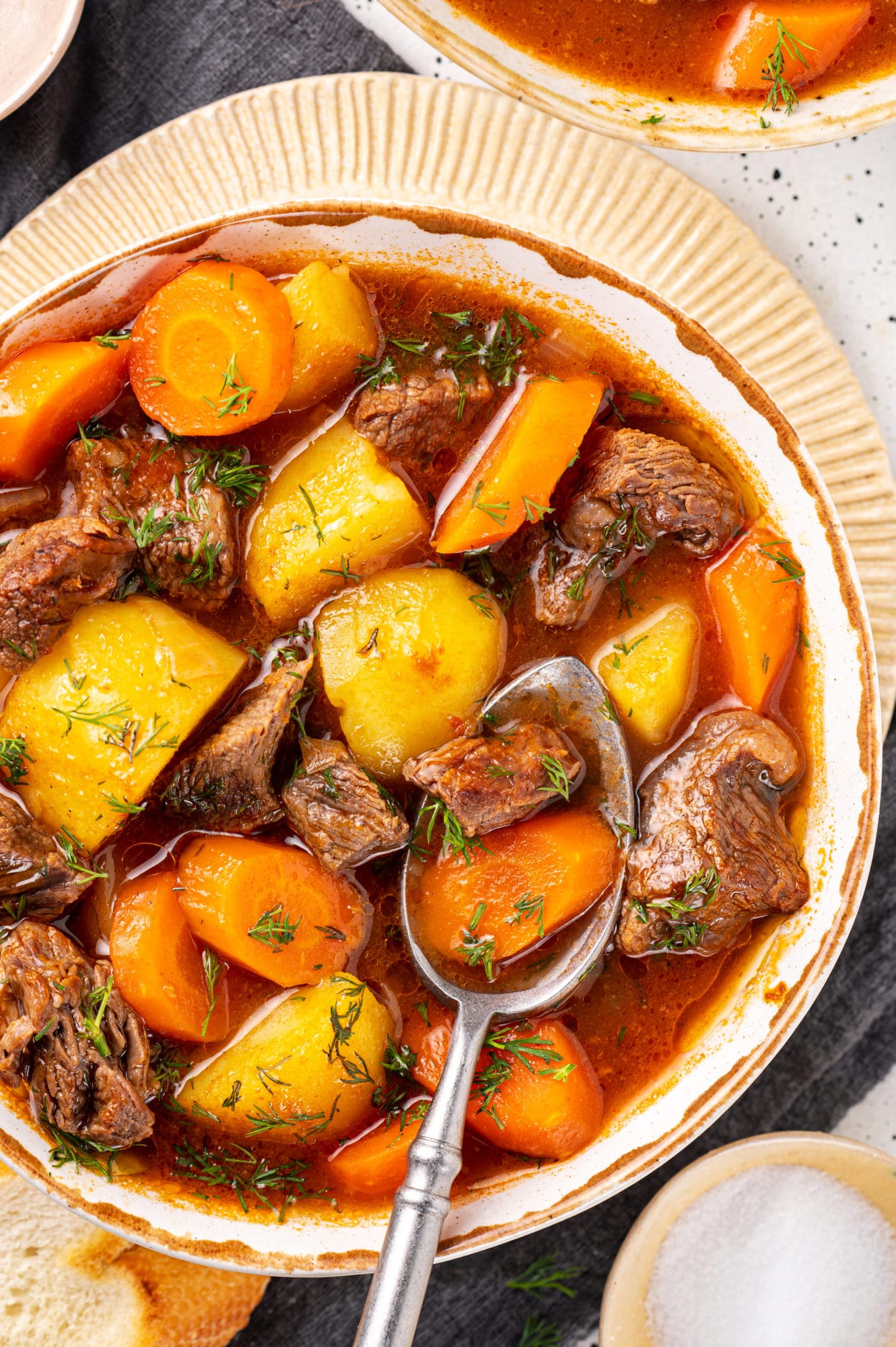 a beige plate with a white bowl on top of it filled with a meat beef stew and a spoon.