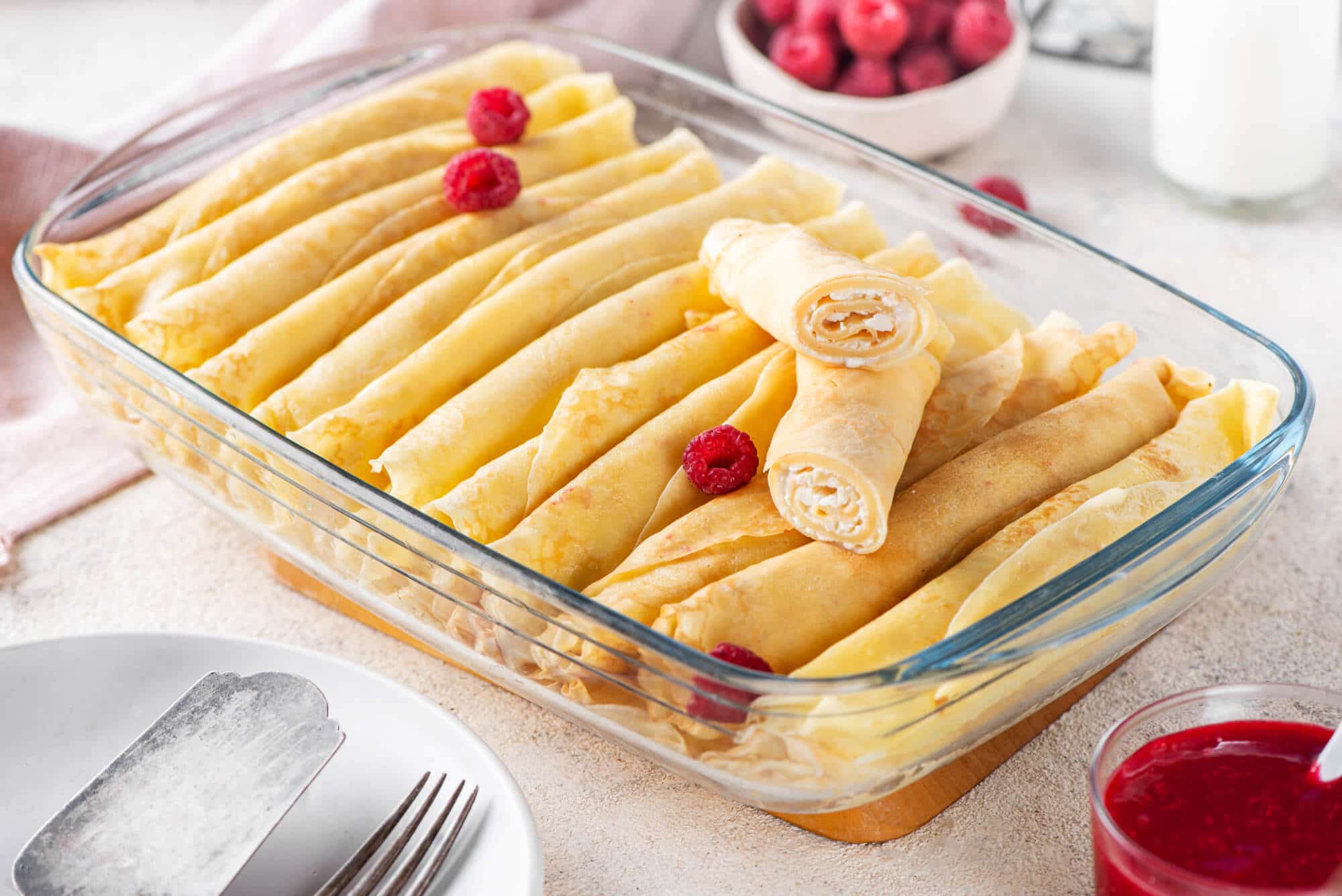 filled-sweet-crepes-in-a-glass-baking-dish-with-raspberries-on-top