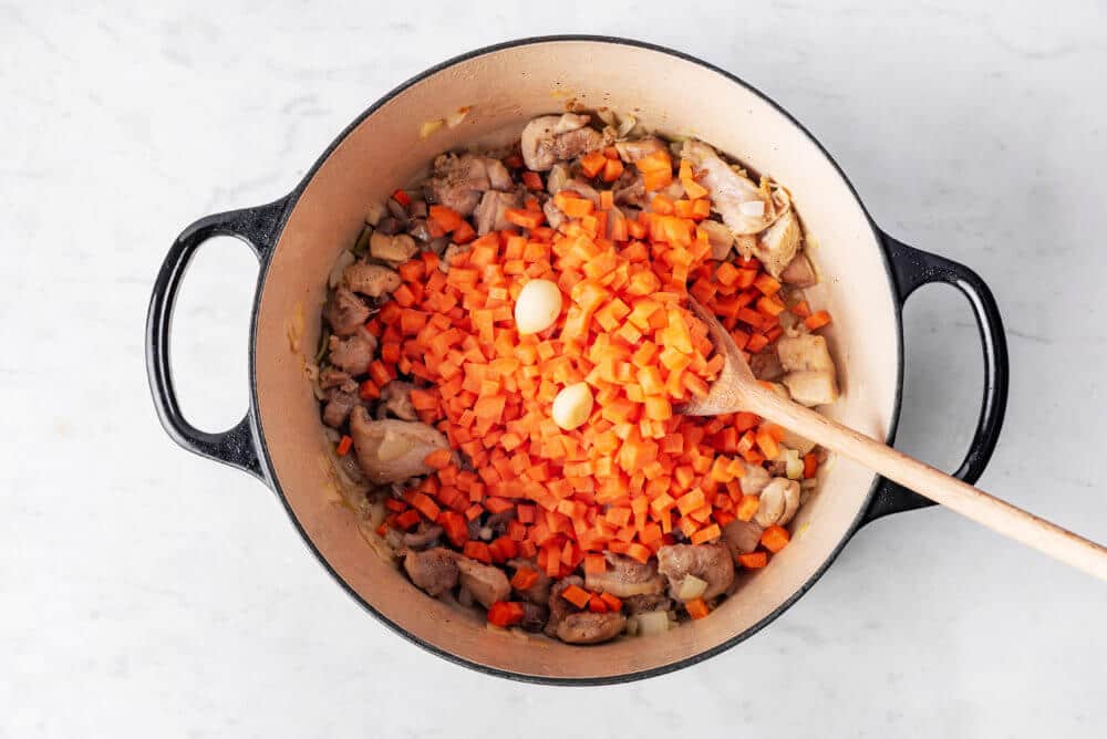 Garlic added atop sauteing plov chicken and carrots.