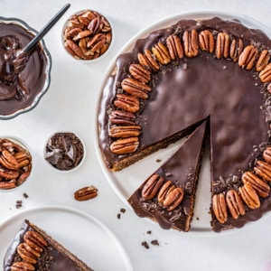 pecan-torte-on-a-white-plate with-bowls-of-chocolate-and-walnuts-on-the-side