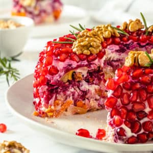 pomegranate salad side view of layers close up salad on a white plate with walnuts and rosemary decoration on top.