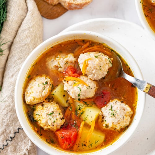 tomato-chicken-soup-in-a-white-bowl-on-a-white-plate-with-a-spoon