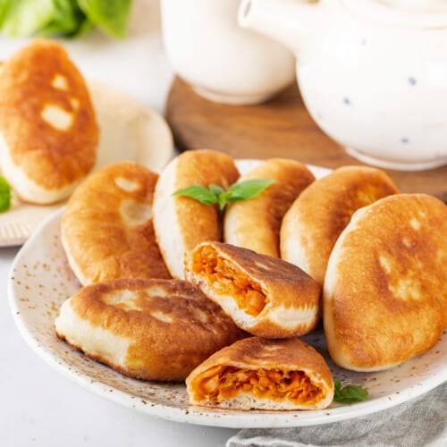 piroshki-with-cabbage-on-a-white-speckled-plate-with-a-teapot-on-a-wooden-board