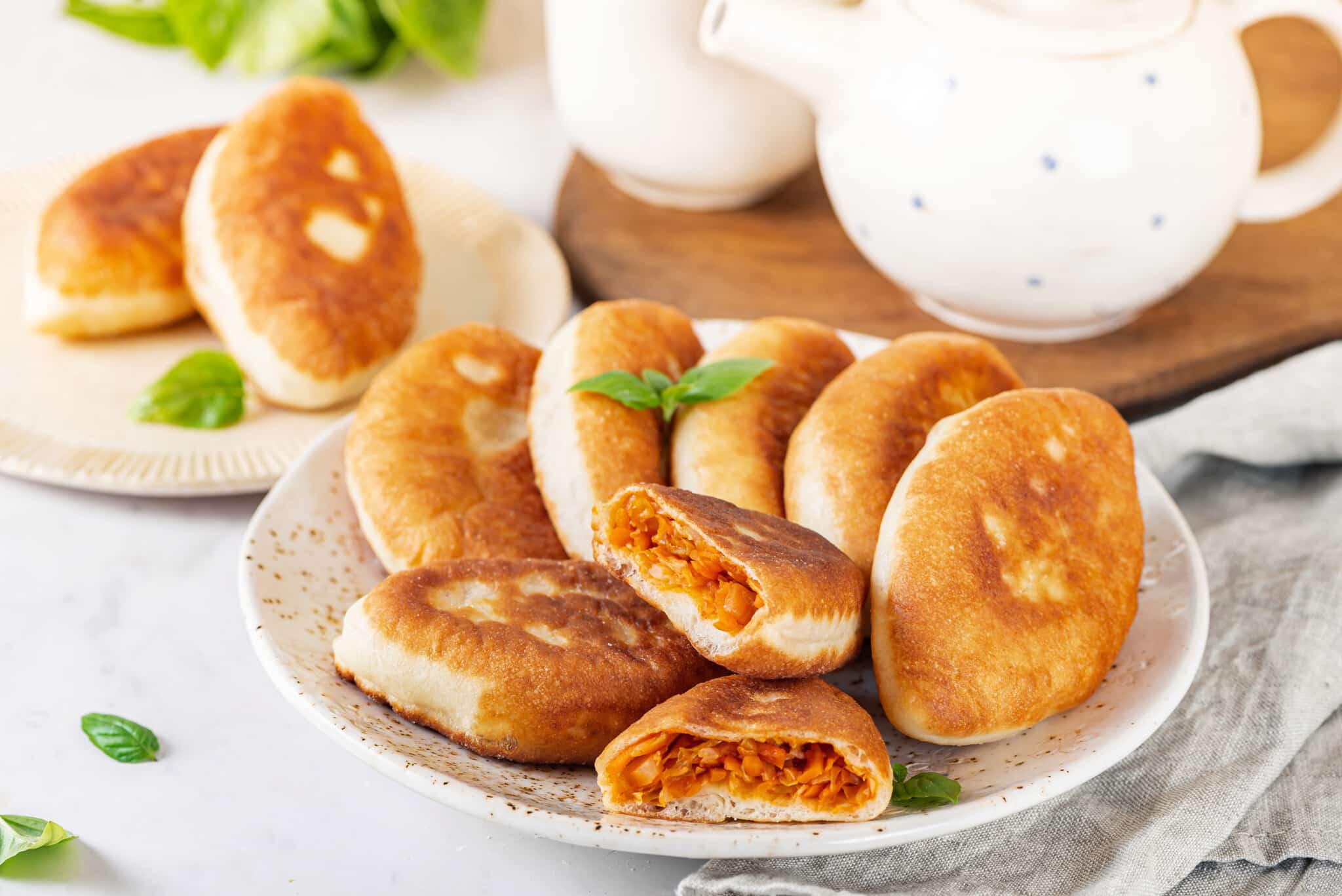 piroshki-with-cabbage-on-a-white-speckled-plate-with-a-teapot-on-a-wooden-board