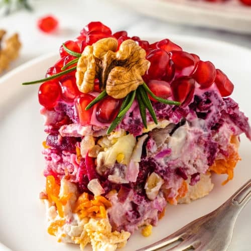 a piece of layered salad with a walnut and rosemary on top on a white plate with a fork.