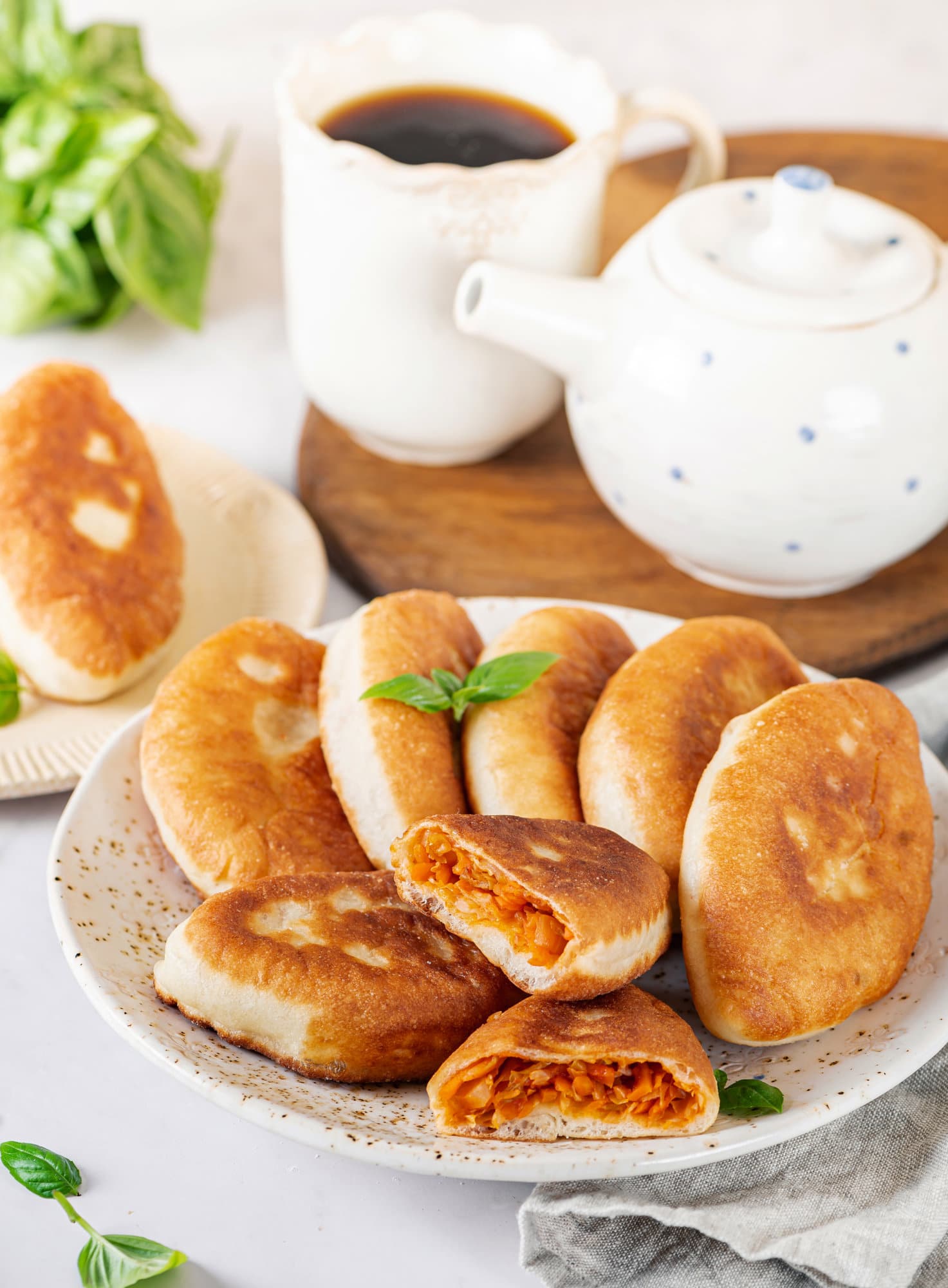 piroshki-with-cabbage-on-a-white-speckled-plate-with-a-teapot-and-a-mug-of-tea-in-the-background-on-a-wooden-board