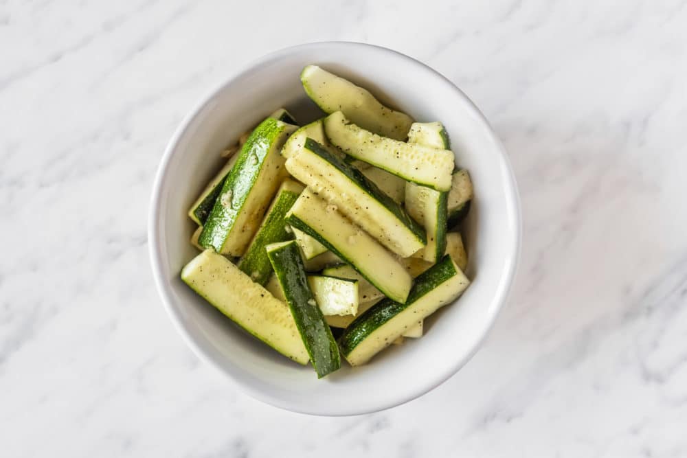 Zucchini slices with marinade in a white bowl.