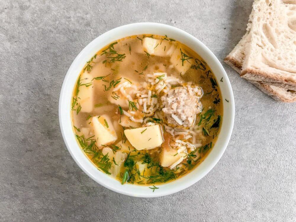 chicken meatball soup in a white bowl with bread slices on the side.