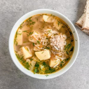 chicken meatball soup in a white bowl with bread slices on the side.