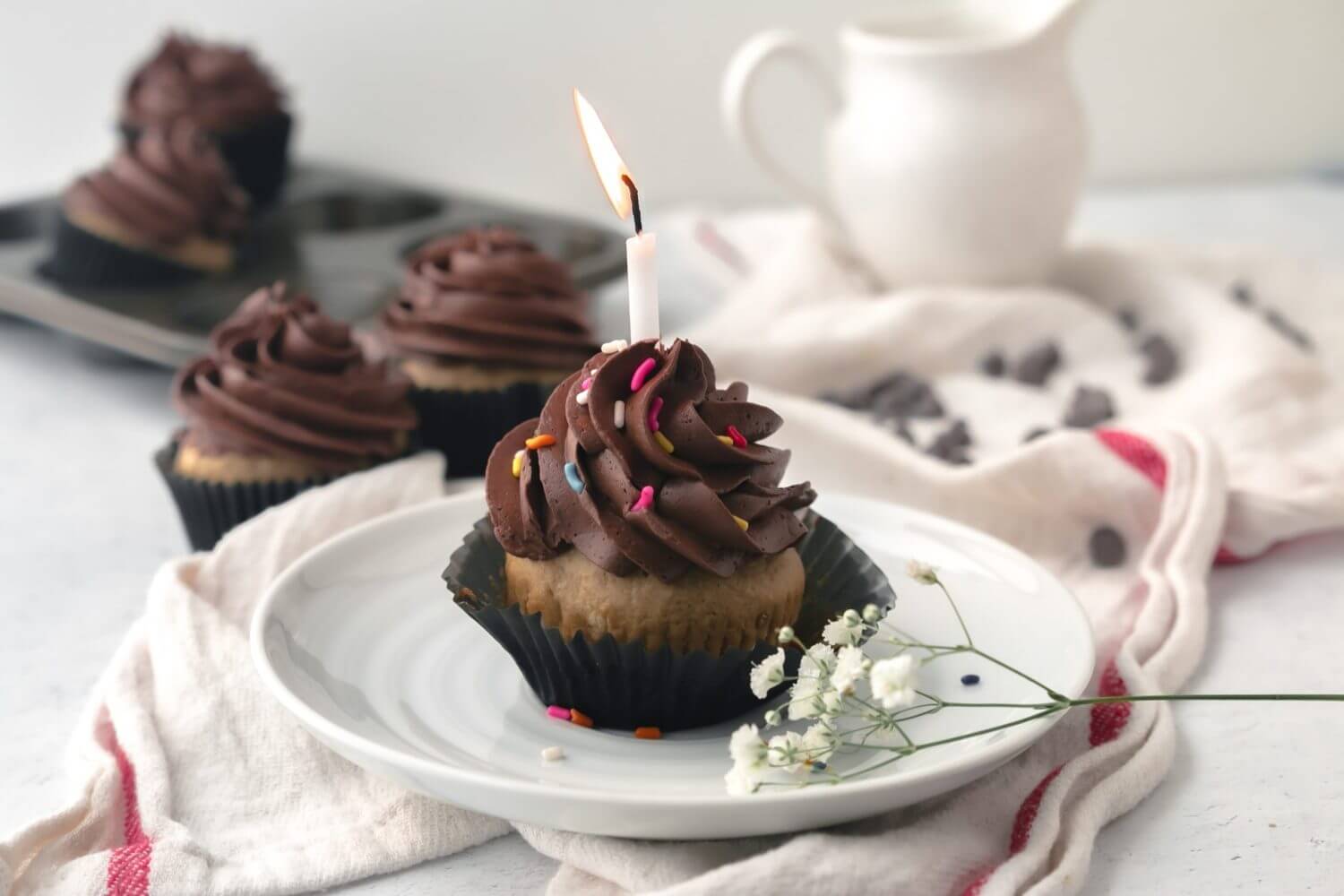 Coffee cupcake with a candle on a white plate on a towel with flowers.