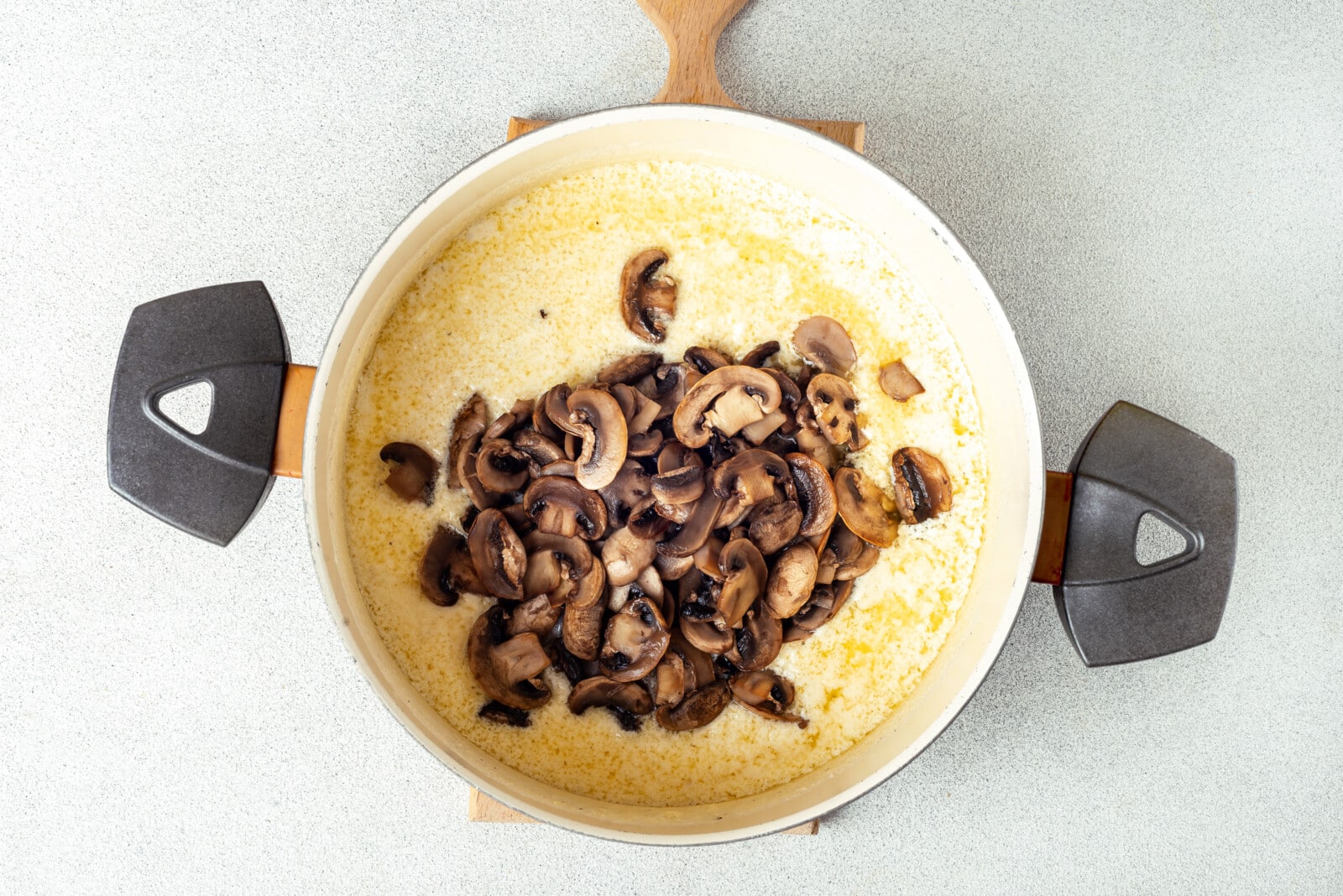 Adding mushrooms to alfredo sauce in a pot.