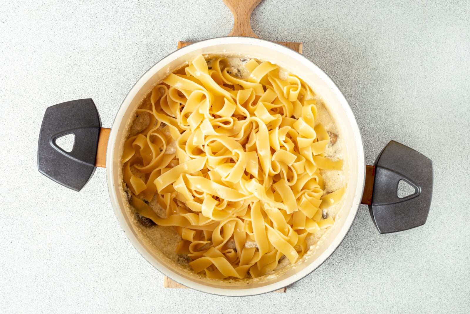 Adding pasta to mushrooms and alfredo sauce.