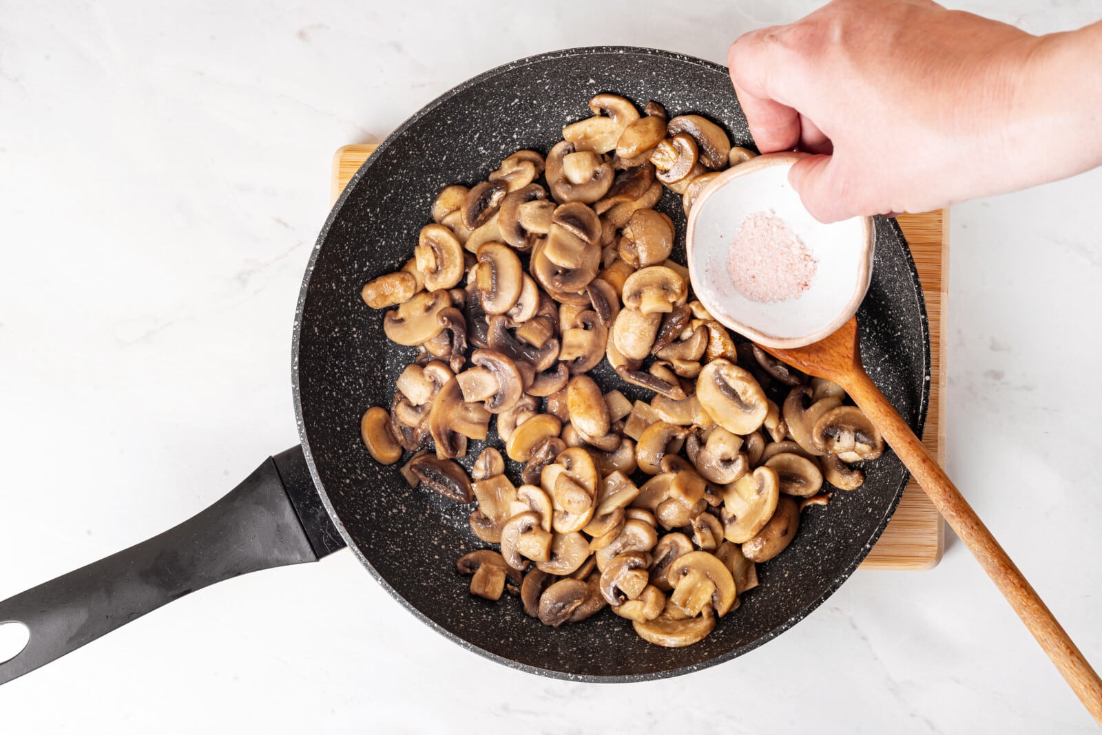 Adding salt to a skillet with sautéed mushrooms.