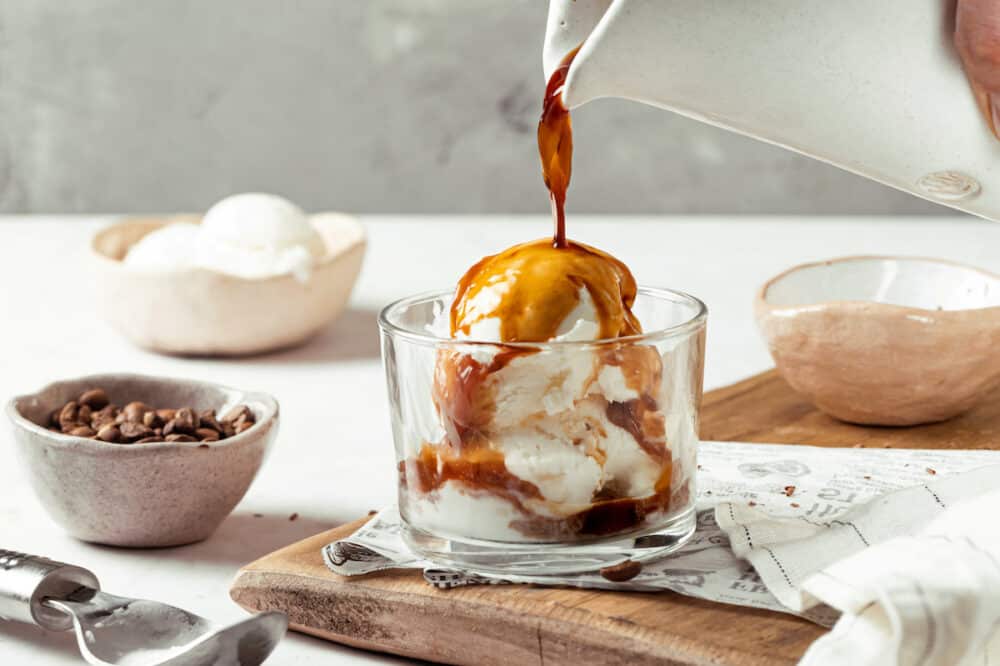 affogato with espresso dripping on top from a white pitcher in to a glass cup with scoops of icecream.