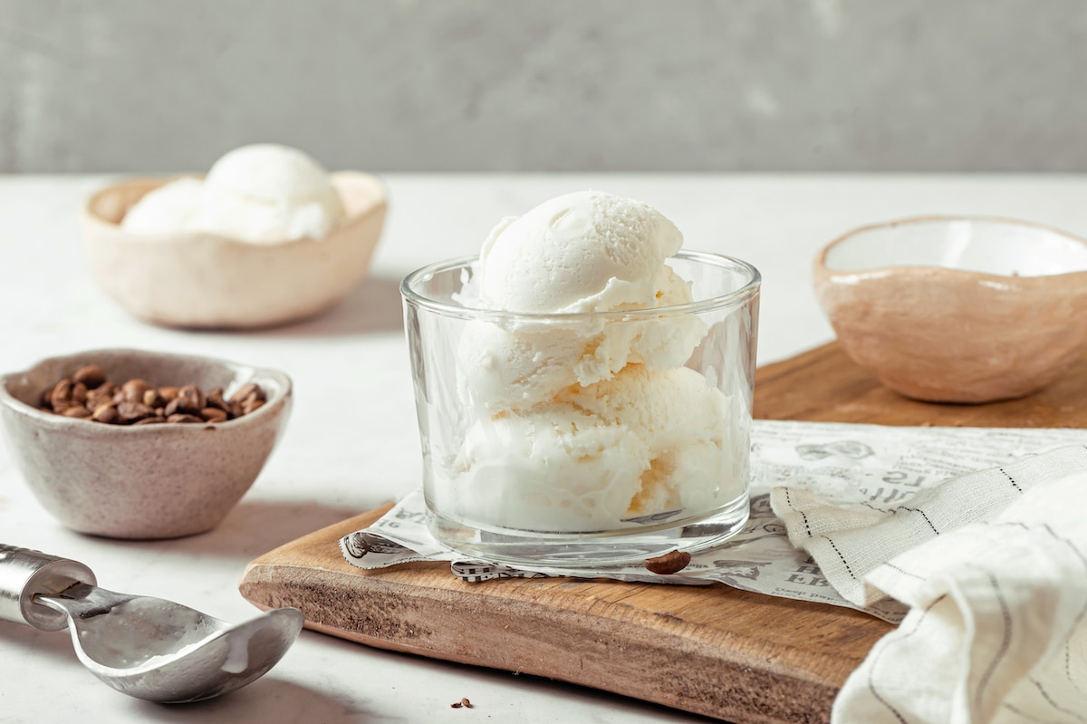 a jar of vanilla ice cream on a wooden board, beside a small bowl of coffee beans