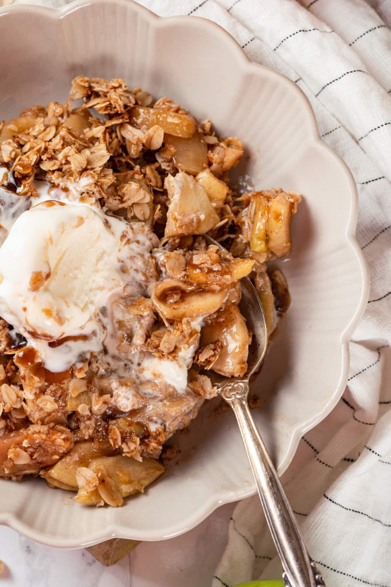 Apple crisp in a white bowl with a spoon, served with icecream.