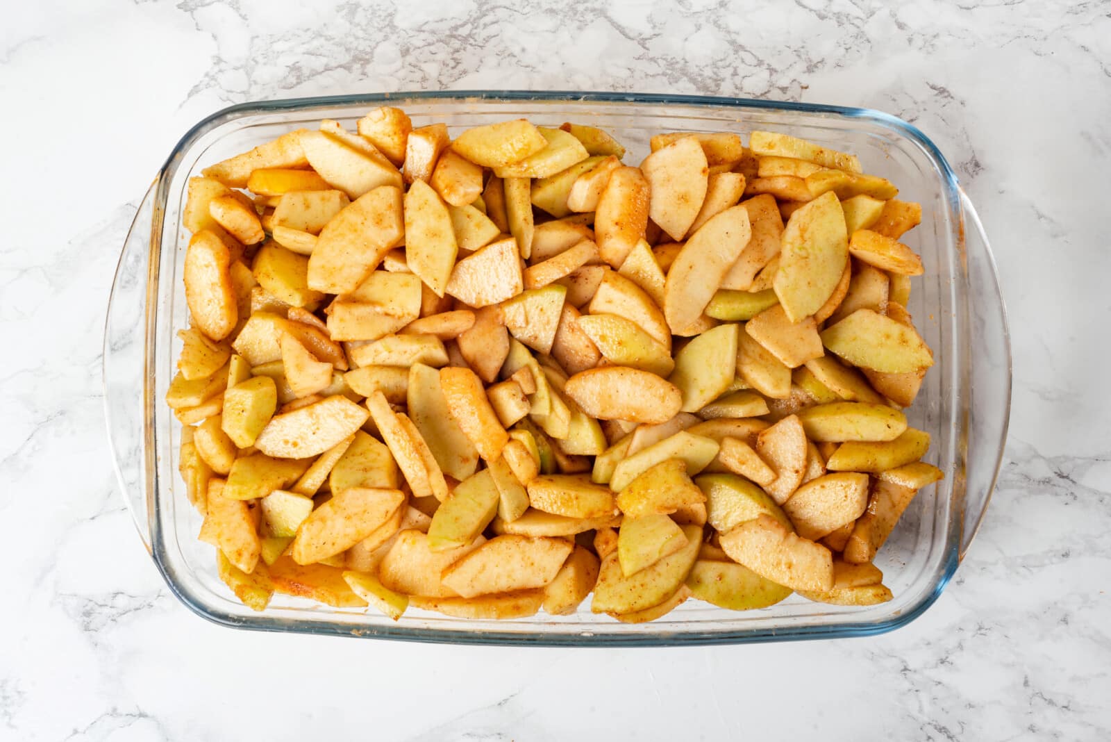 Apples seasoned and mixed to bake in a glass pan.