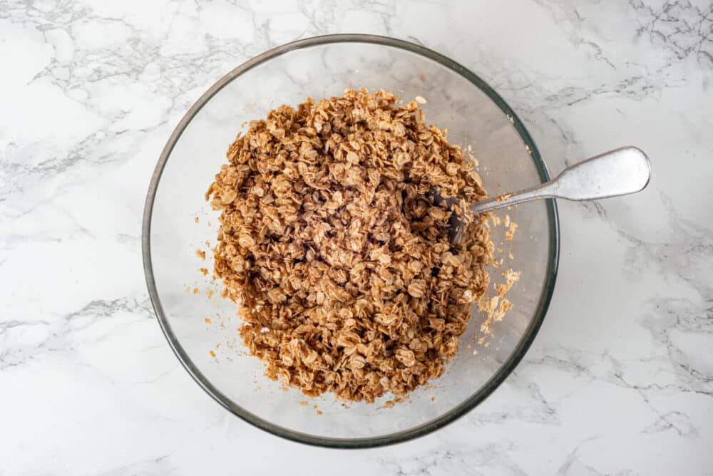 Mixed apple crisp topping in a glass bowl with a spoon.