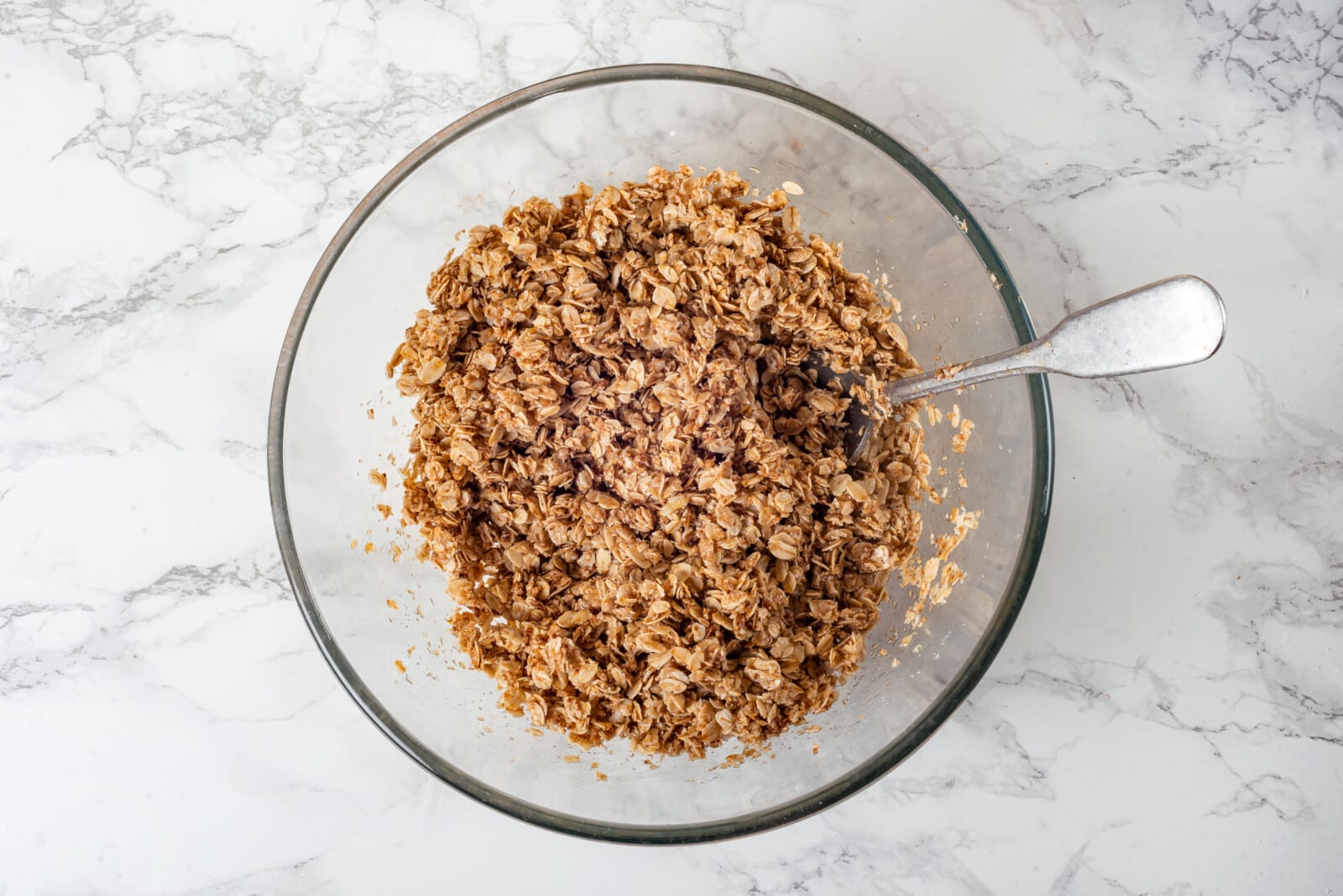 Mixed apple crisp topping in a glass bowl with a spoon.