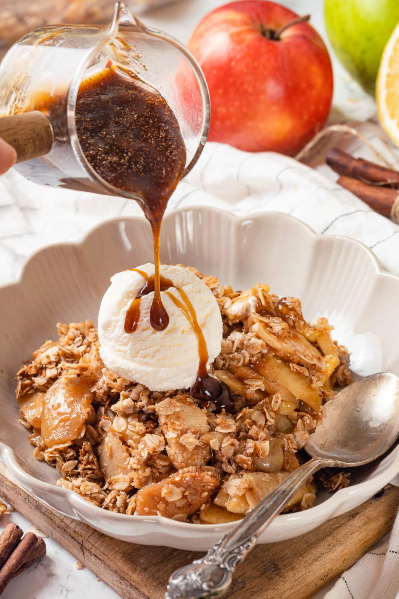 Apple crisp with a scoop of ice cream in a bowl, pouring caramel sauce on top for serving.