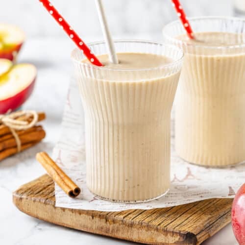 Apple pie smoothie in glasses with straws, and cinnamon on the side.