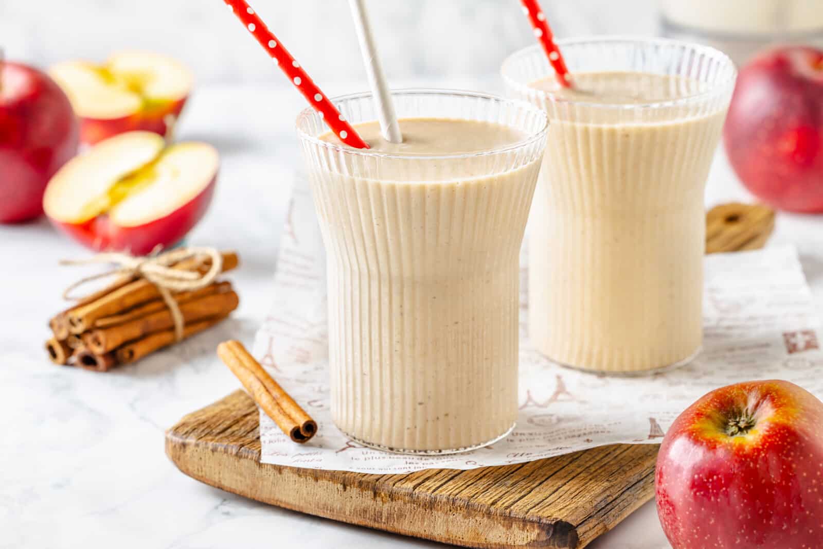 Apple pie smoothie in glasses with straws, and cinnamon on the side.