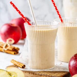 Apple pie smoothie in rimmed glasses with a red and white straws.