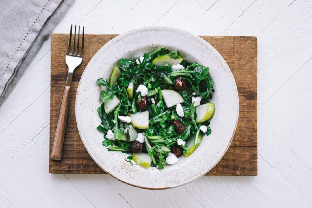 arugula-pear-salad-in-a-white-bowl-on-a-wooden-board-with-a-fork