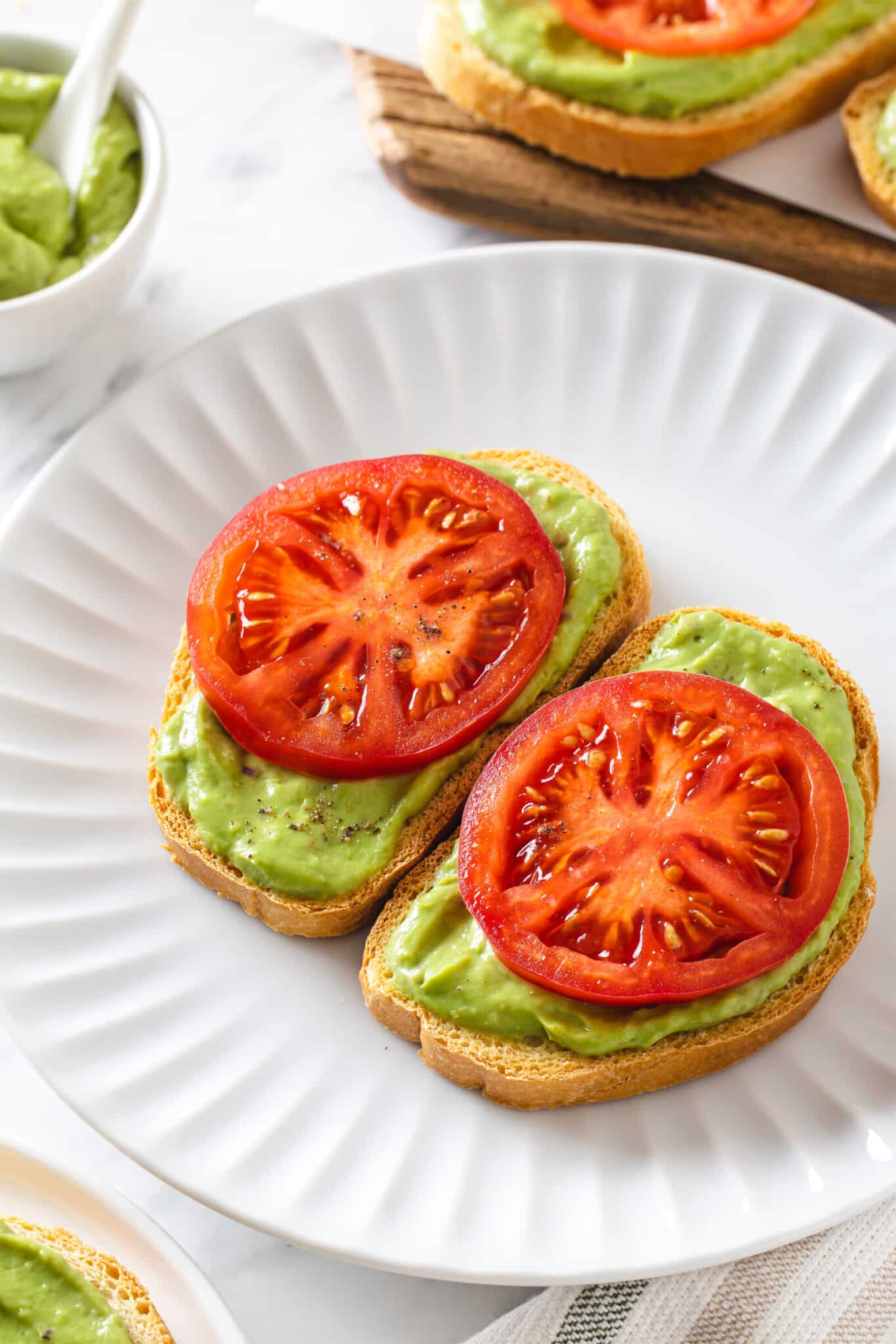 avocado appetizers on a white plate with a large tomato slice on each of them.