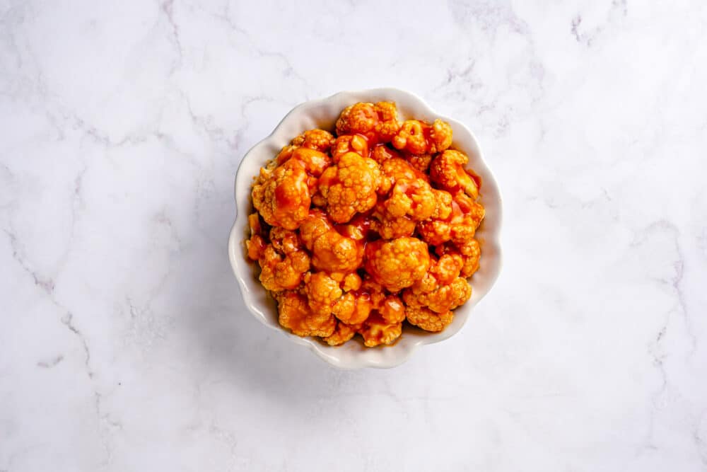 baked cauliflower roasted florets mixed in buffalo sauce in a white bowl.