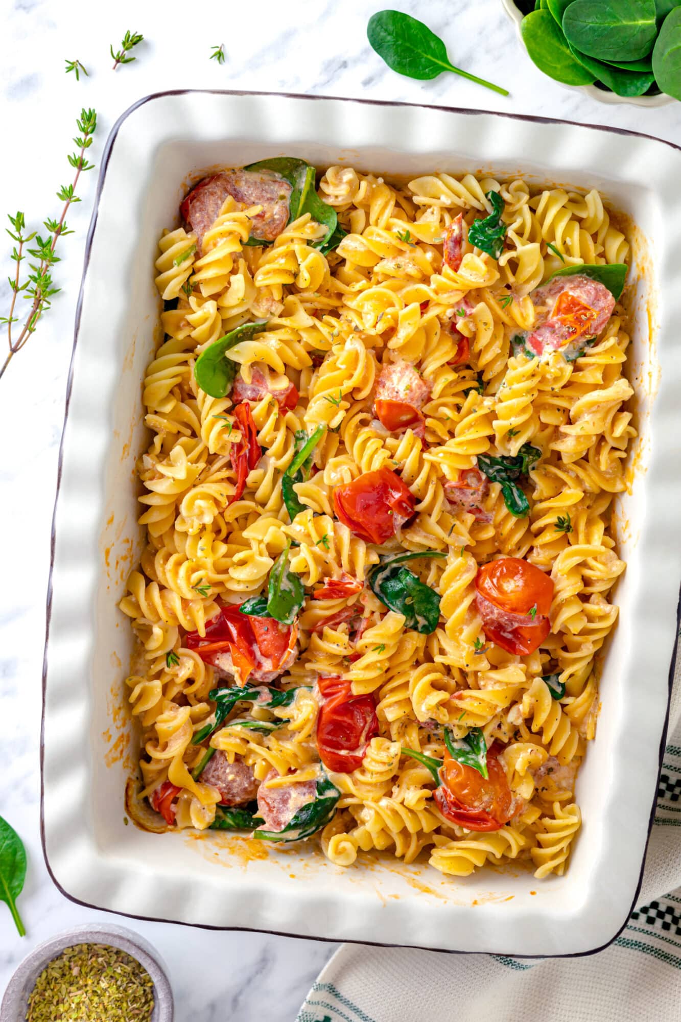 a large baking dish full of baked feta pasta with cherry tomatoes and spinach scattered throughout